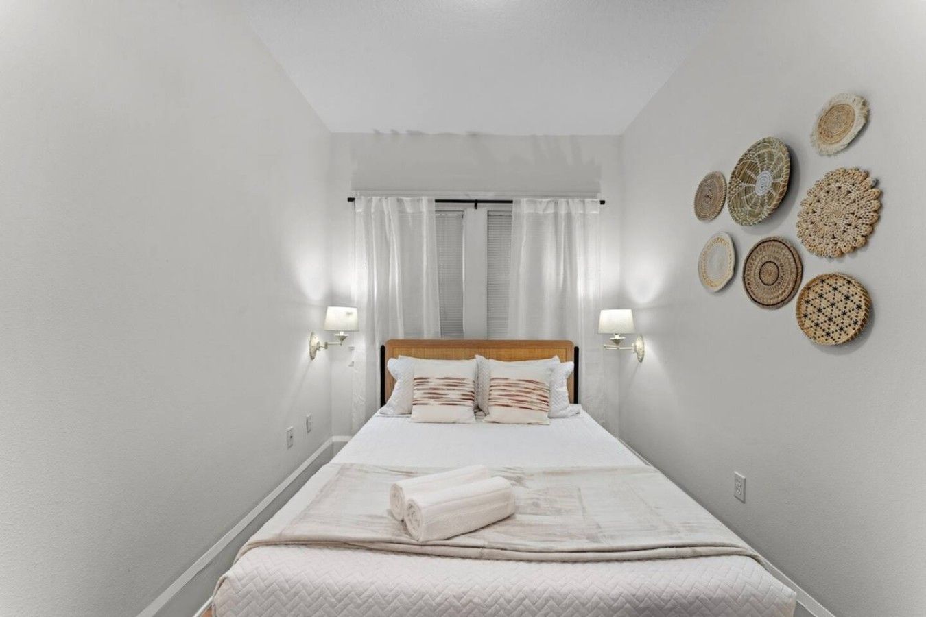 Een slaapkamer met een bed, gordijnen, wandlampen en decoratieve muurkunst.
