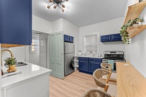 A modern kitchen with white cabinetry, a stainless steel refrigerator, a wooden dining table, and a built-in oven. - 2BR Lake Toho Waterfront Retreat | Fish • Relax (Nutley)
