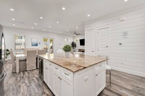 A modern kitchen with white cabinetry, a granite countertop, and a dining area with a table and chairs. - 7BR Beachside Retreat | Pool • Billiards • Miramar (Miramar Beach)