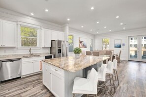 A modern kitchen with white cabinetry, stainless steel appliances, and a central island with bar stools. - 7BR Beachside Retreat | Pool • Billiards • Miramar (Miramar Beach)