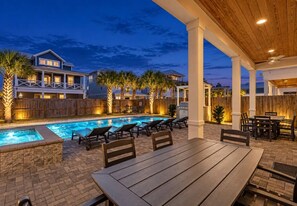 A poolside area with lounge chairs and a table, surrounded by a wooden fence and palm trees. - 7BR Beachside Retreat | Pool • Billiards • Miramar (Miramar Beach)