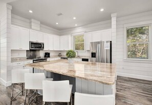 A modern kitchen with white cabinetry, a granite countertop island, and bar stools. - 7BR Beachside Retreat | Pool • Billiards • Miramar (Miramar Beach)