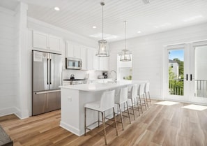 A modern kitchen with white cabinetry, stainless steel appliances, and a central island with bar stools. - 7BR Beach Escape | Private Pool + Billiards (Miramar Beach)
