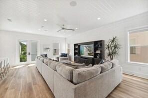 A spacious living room with a large sectional sofa, a flat-screen TV, and a ceiling fan. - 7BR Beach Escape | Private Pool + Billiards (Miramar Beach)