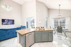 A modern kitchen with a granite countertop, grey cabinets, and a built-in sink. - Family Disney Getaway | 5BR • Pool • Near Magic (Kissimmee)