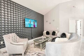 A modern living room with a geometric patterned wall, a television, and a sofa with decorative pillows. - Family Disney Getaway | 5BR • Pool • Near Magic (Kissimmee)