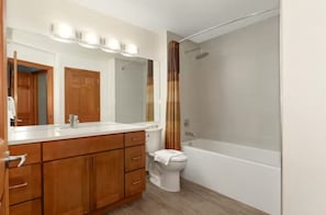 Une salle de bain avec des meubles en bois, des toilettes blanches, une baignoire et un rideau de douche.