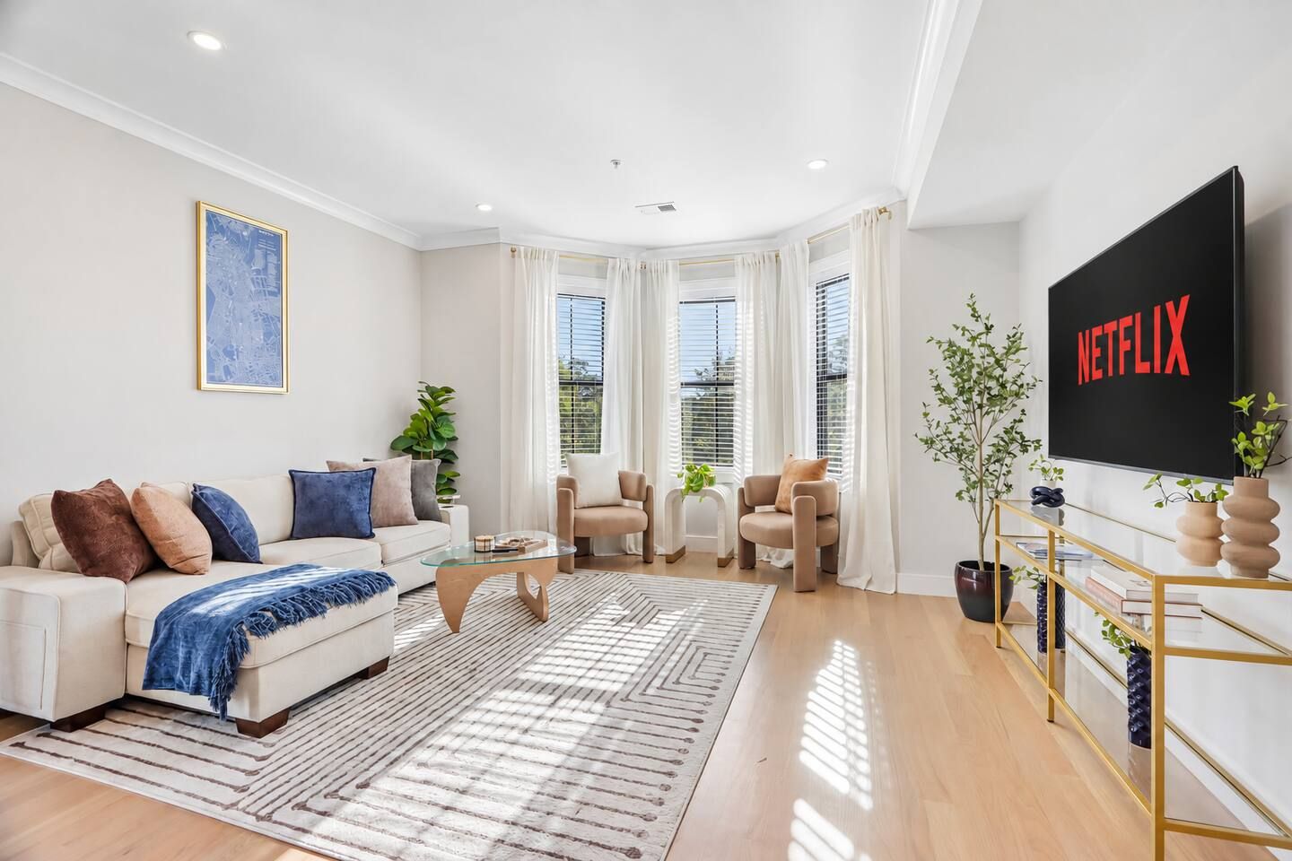 Een moderne woonkamer met een bank, fauteuils, een salontafel en een aan de muur bevestigde televisie.
