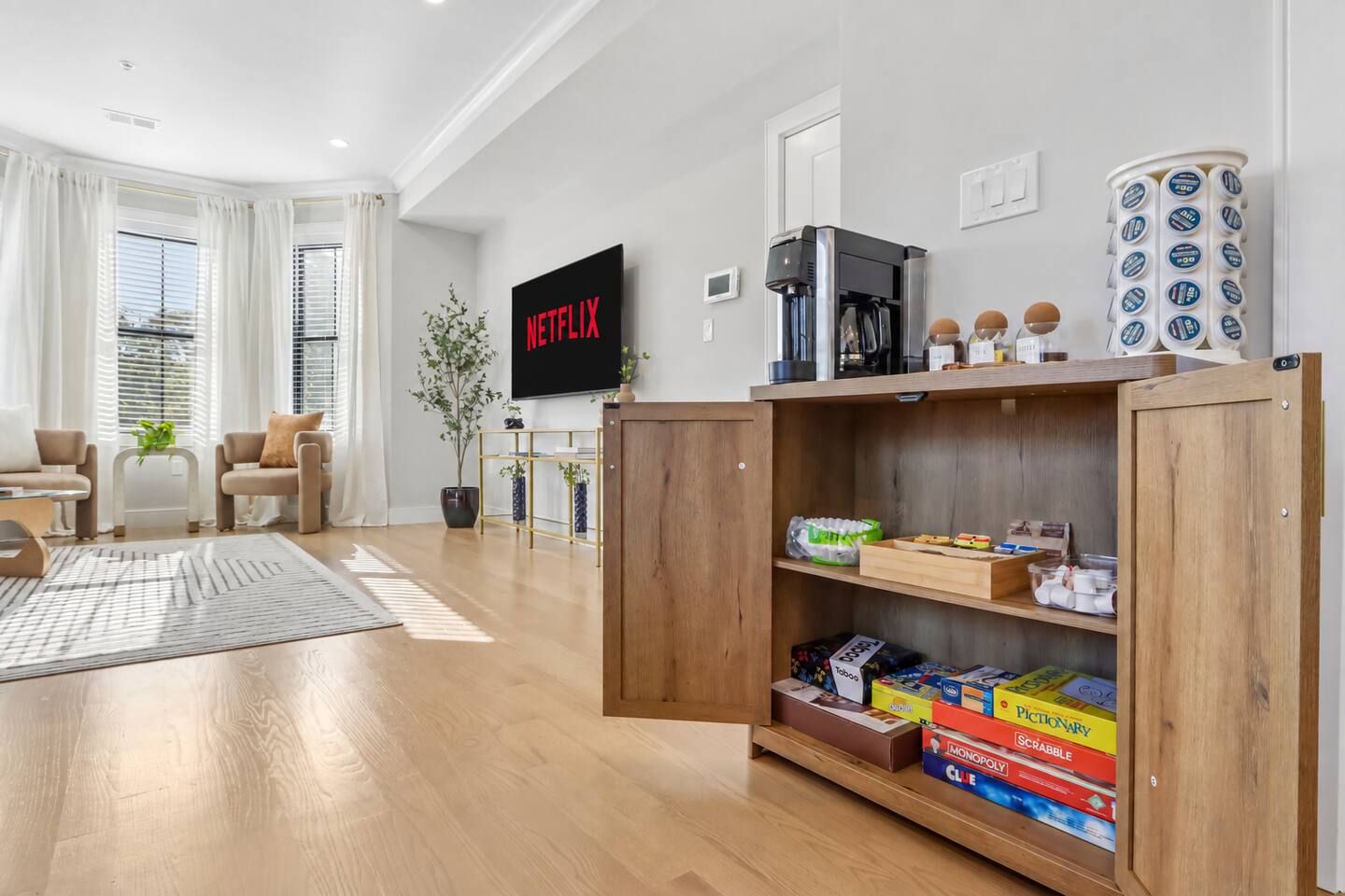 A modern living room with a flat-screen TV, wooden shelves with board games, and a coffee machine.