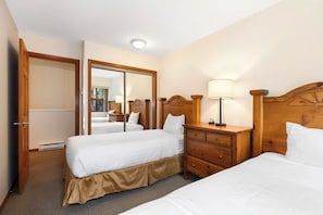 Camera d'albergo con due letti, una testiera in legno, un comodino con una lampada e un grande specchio.