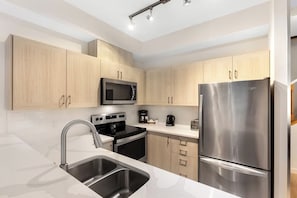 Una cocina moderna con armarios de madera clara, electrodomésticos de acero inoxidable y encimera de mármol blanco.