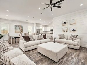 Amplia sala de estar con sofá modular, reposapiés y comedor con mesa y sillas.