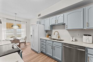 Una cocina moderna con armarios grises, un lavavajillas de acero inoxidable y un comedor con mesa y sillas.