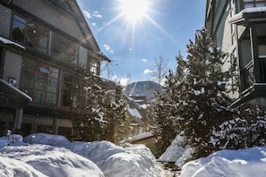 Una strada coperta di neve con edifici su entrambi i lati, cielo sereno e una montagna sullo sfondo.