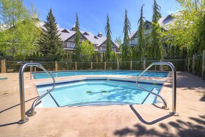 Una piscina con ringhiere metalliche, circondata da alberi e edifici con tetti spioventi.