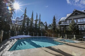 Una piscina con acqua cristallina e blu, circondata da alberi alti e un edificio con tetto spiovente.
