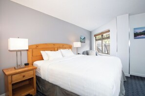 A hotel room with a large bed, a wooden headboard, a nightstand with a lamp, a window with a view, and a painting on the wall. - Lake Placid Lodge | 2 Bedroom | Pool access (Whistler)
