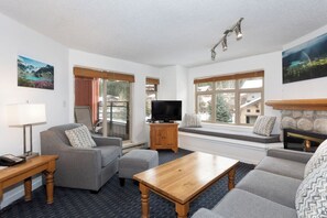Ein Wohnzimmer mit Sofa, Hocker, Couchtisch, Fernseher und Kamin.