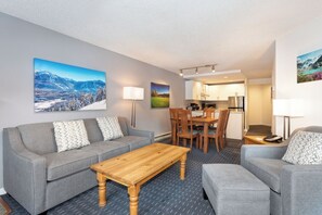 A modern hotel room with a grey sofa, a wooden coffee table, and a dining area with a table and chairs. - Lake Placid Lodge | 2 Bedroom | Pool access (Whistler)