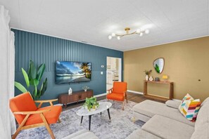 A living room with a television, a sofa, two armchairs, a coffee table, and a console table with decorative items. - Boho Lakeside Retreat | Walk to Lake Toho (Kissimmee)