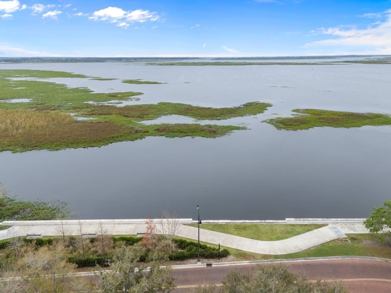 Una extensa masa de agua con zonas verdes y un camino de hormigón que lleva a un puente.