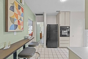 A kitchen with a refrigerator, oven, and a dining area with a bench and a table. - Boho Lakeside Retreat | Walk to Lake Toho (Kissimmee)