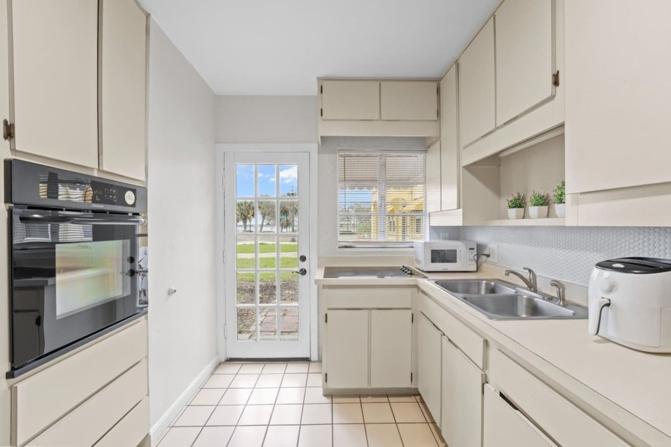 A compact kitchen with a built-in oven, a microwave, a toaster, and a window with blinds.