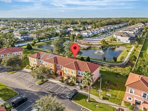 A residential area with multiple two-story buildings, a parking lot, and a body of water with a fountain. - Lake Berkley Retreat | Pool • Fishing • Clubhouse (Kissimmee)