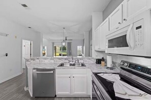 A modern kitchen with white cabinetry, a marble countertop, stainless steel appliances, and a view to the outdoors. - Lake Berkley Retreat | Pool • Fishing • Clubhouse (Kissimmee)