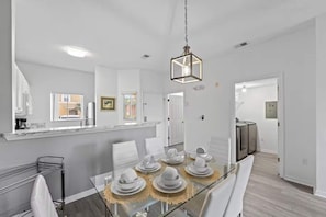 A modern kitchen with white cabinets, a marble countertop, and a dining area with a glass table set for four. - Lake Berkley Retreat | Pool • Fishing • Clubhouse (Kissimmee)