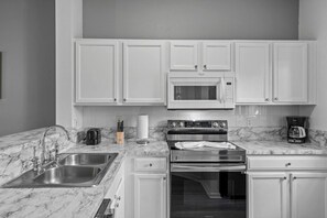 A modern kitchen with white cabinetry, a stainless steel sink, a microwave, a stove, and a coffee maker. - Lake Berkley Retreat | Pool • Fishing • Clubhouse (Kissimmee)