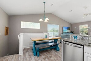 A kitchen with a built-in dishwasher, a wooden dining table with benches, and a large window providing natural light. - Your Perfect Beach Getaway | Destin Coastal Home (Destin)