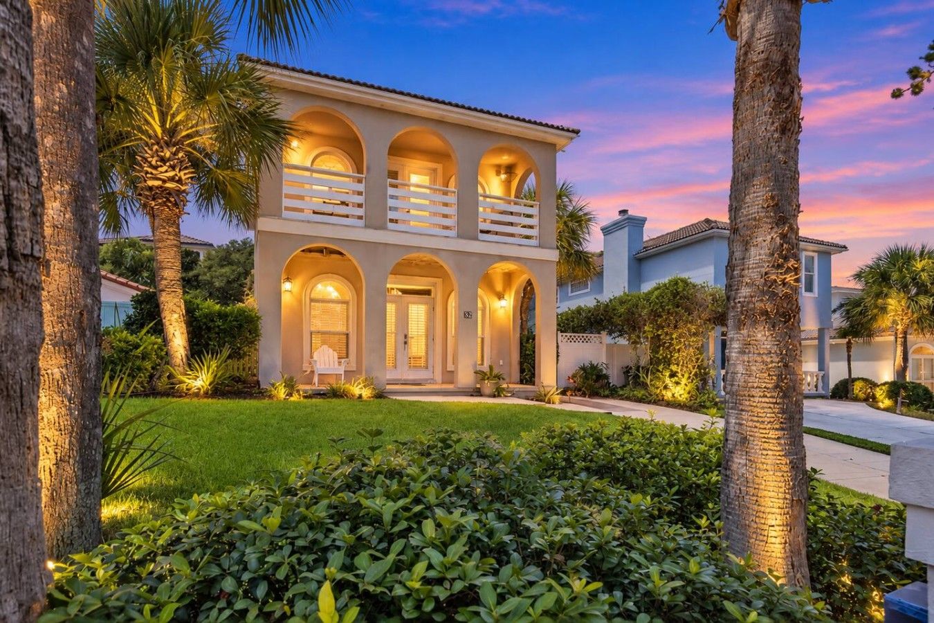 A two-story house with a balcony, surrounded by palm trees and well-maintained landscaping.