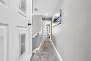 A hallway with a carpeted floor, white doors, and a picture on the wall. - Destin Family Retreat | Private Pool + Beach (Destin)