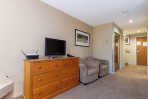 A room with a wooden dresser, a television, a beige armchair, and a framed picture on the wall. - 1 Bedroom Loft | Fireplace | Village Gate House by Whiski Jack (Whistler)
