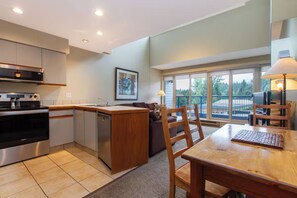 Une cuisine moderne dotée d’un four encastré, d’un lave-vaisselle et d’un îlot central en bois. On y trouve également un coin repas avec une table et des chaises, ainsi qu’une grande fenêtre offrant une vue sur l’extérieur.