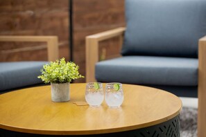 A round wooden table with two glasses of a clear beverage and a small potted plant. - Austins Ember House | Hot Tub • Pit • Ping Pong (Austin)