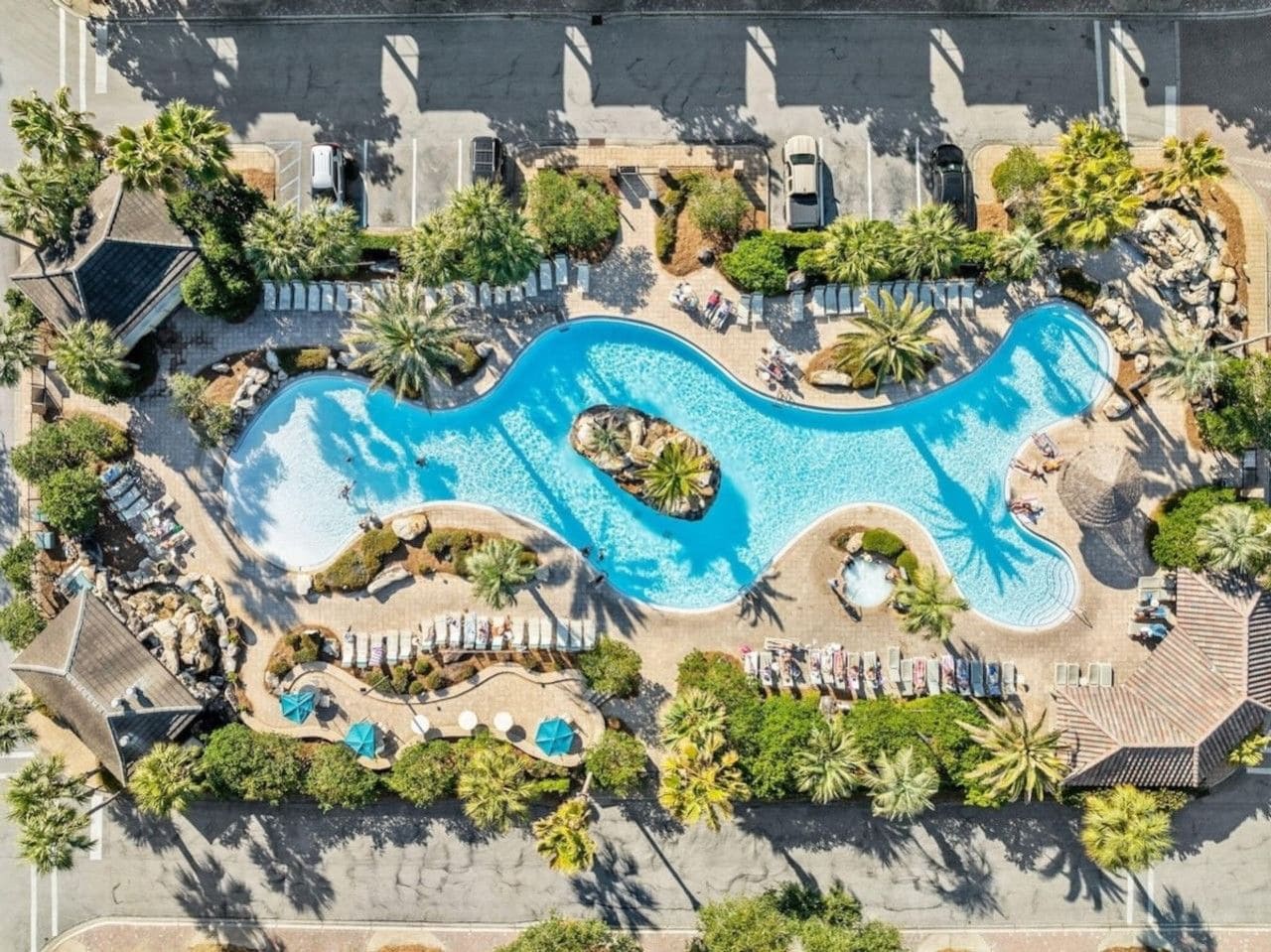 Vue aérienne d’un complexe hôtelier doté d’une grande piscine, d’espaces de détente et de palmiers.