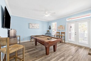 Una sala con piscina y mesa de billar, sillas, televisor y obras de arte en las paredes.