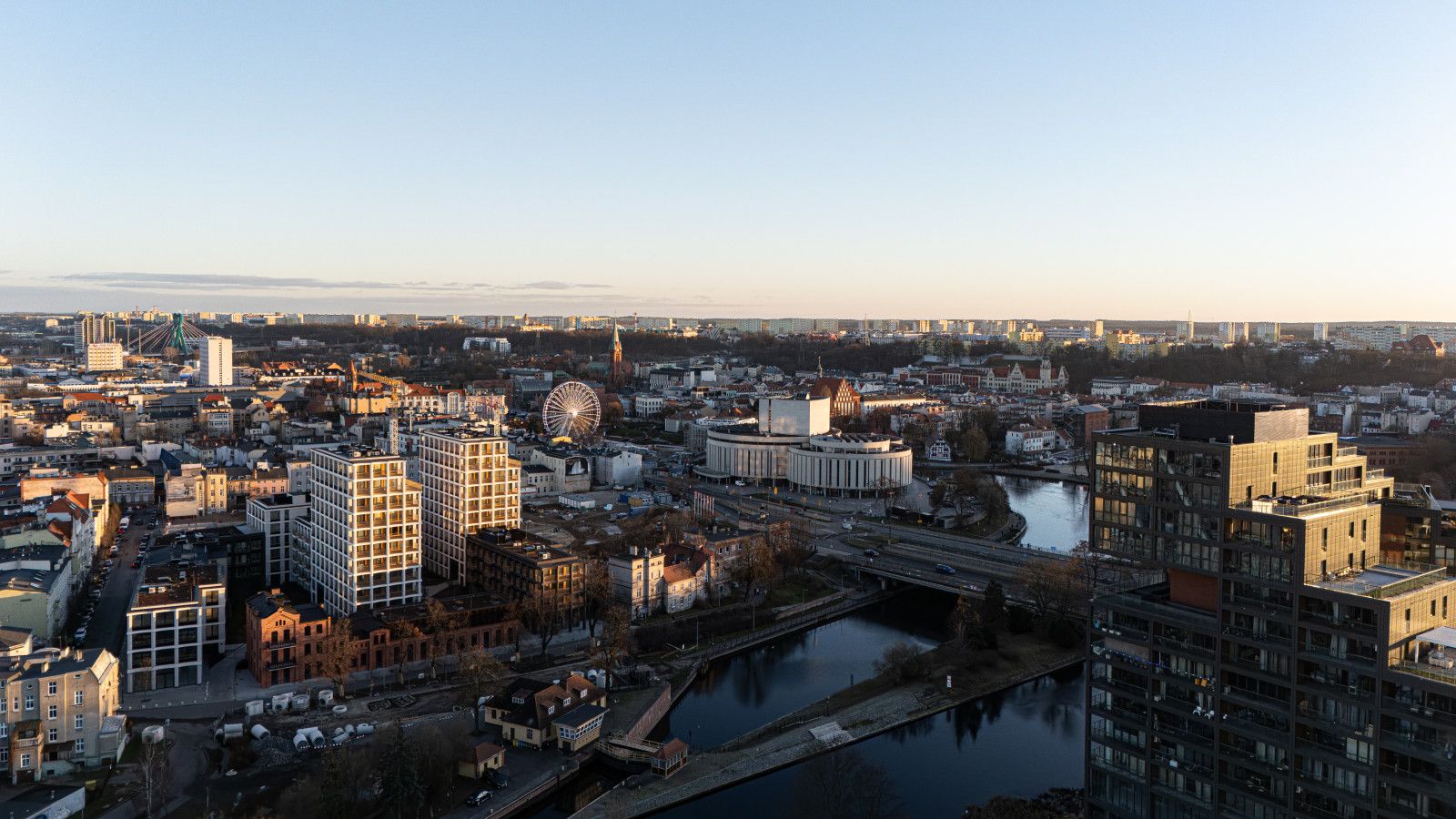 A cityscape with a river, a prominent Ferris wheel, and various buildings including a large circular structure.