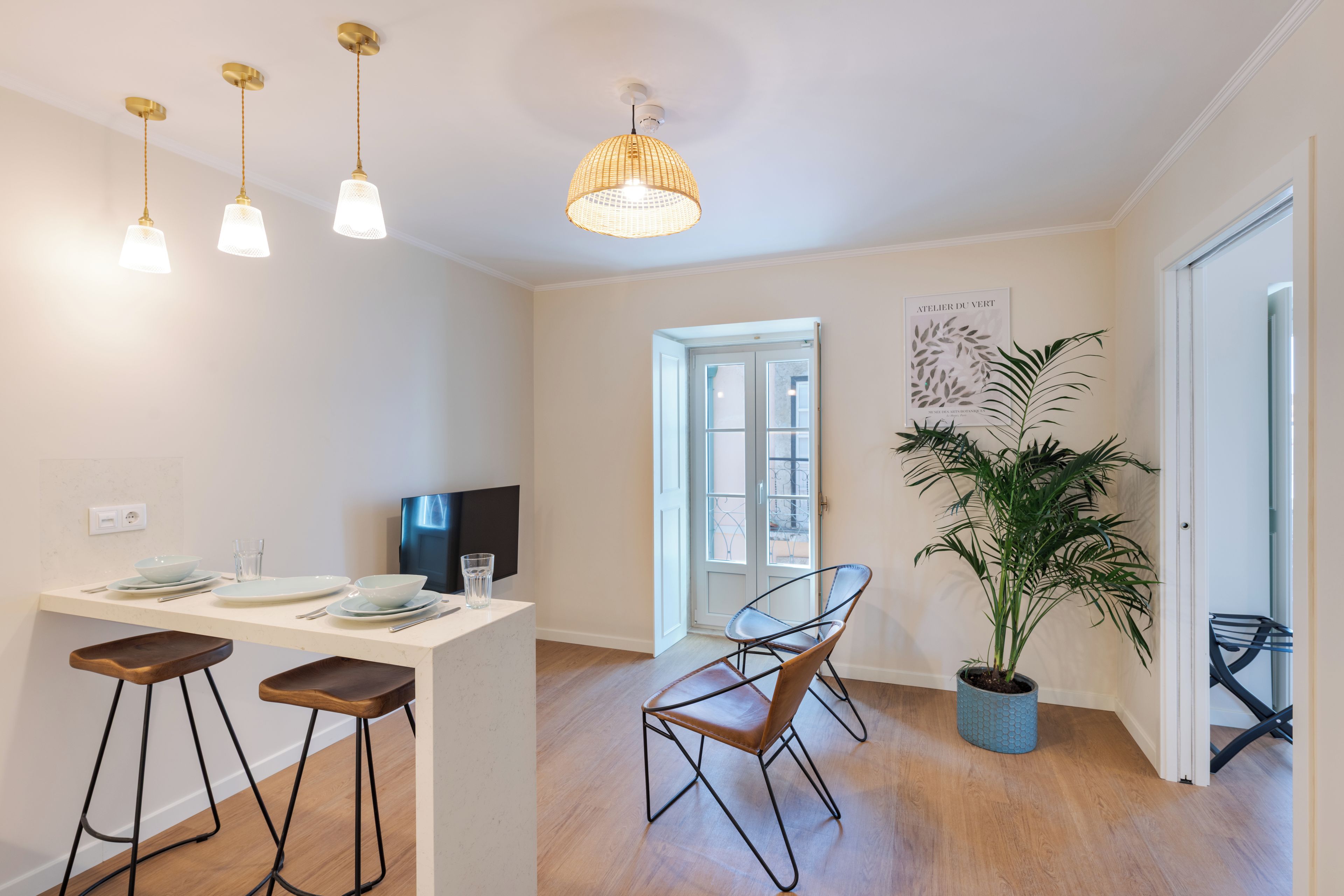 A modern kitchen with a dining area, wooden stools, and a potted plant.