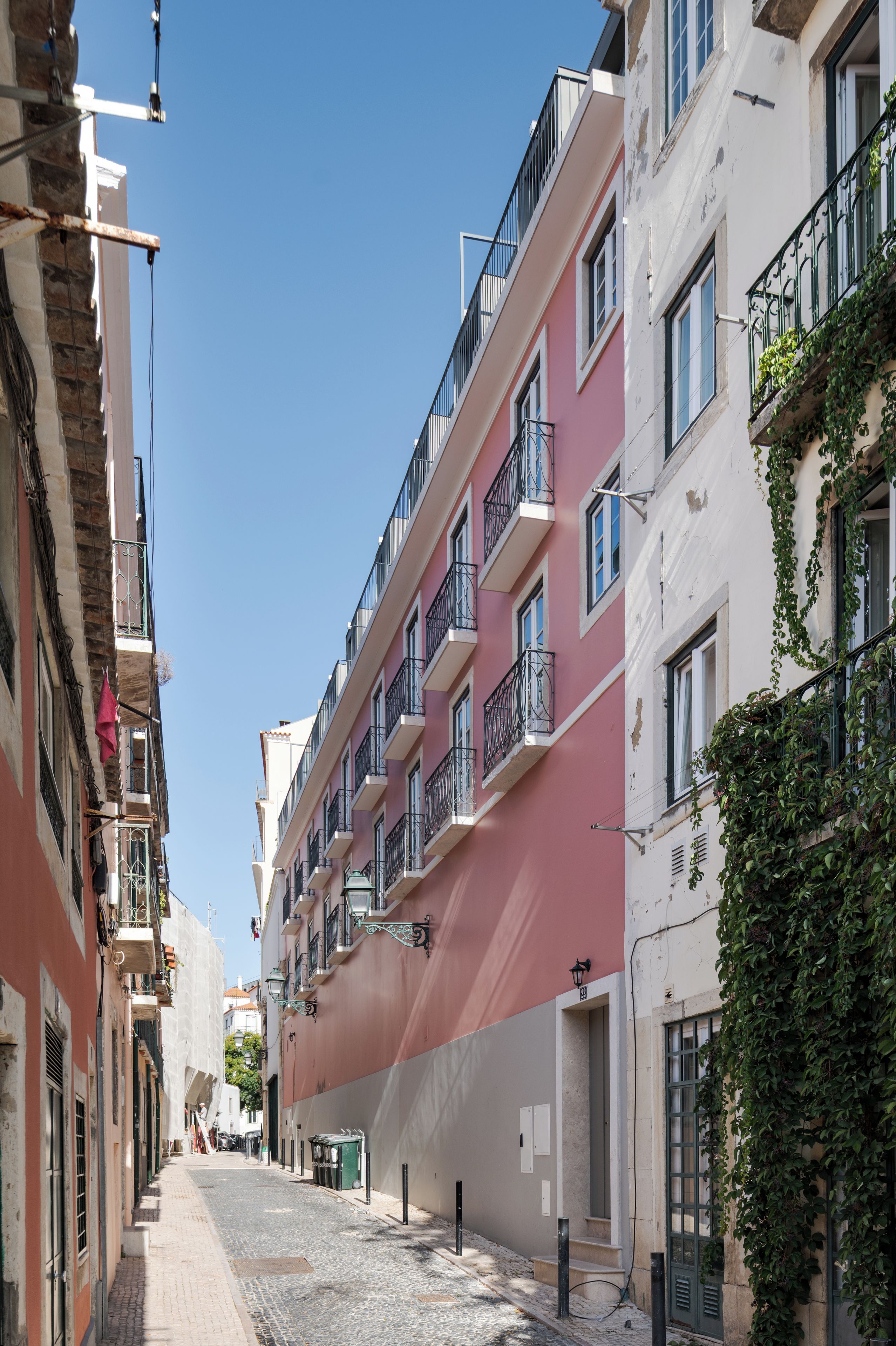 A narrow street lined with multi-story buildings, some with balconies and others with vines.