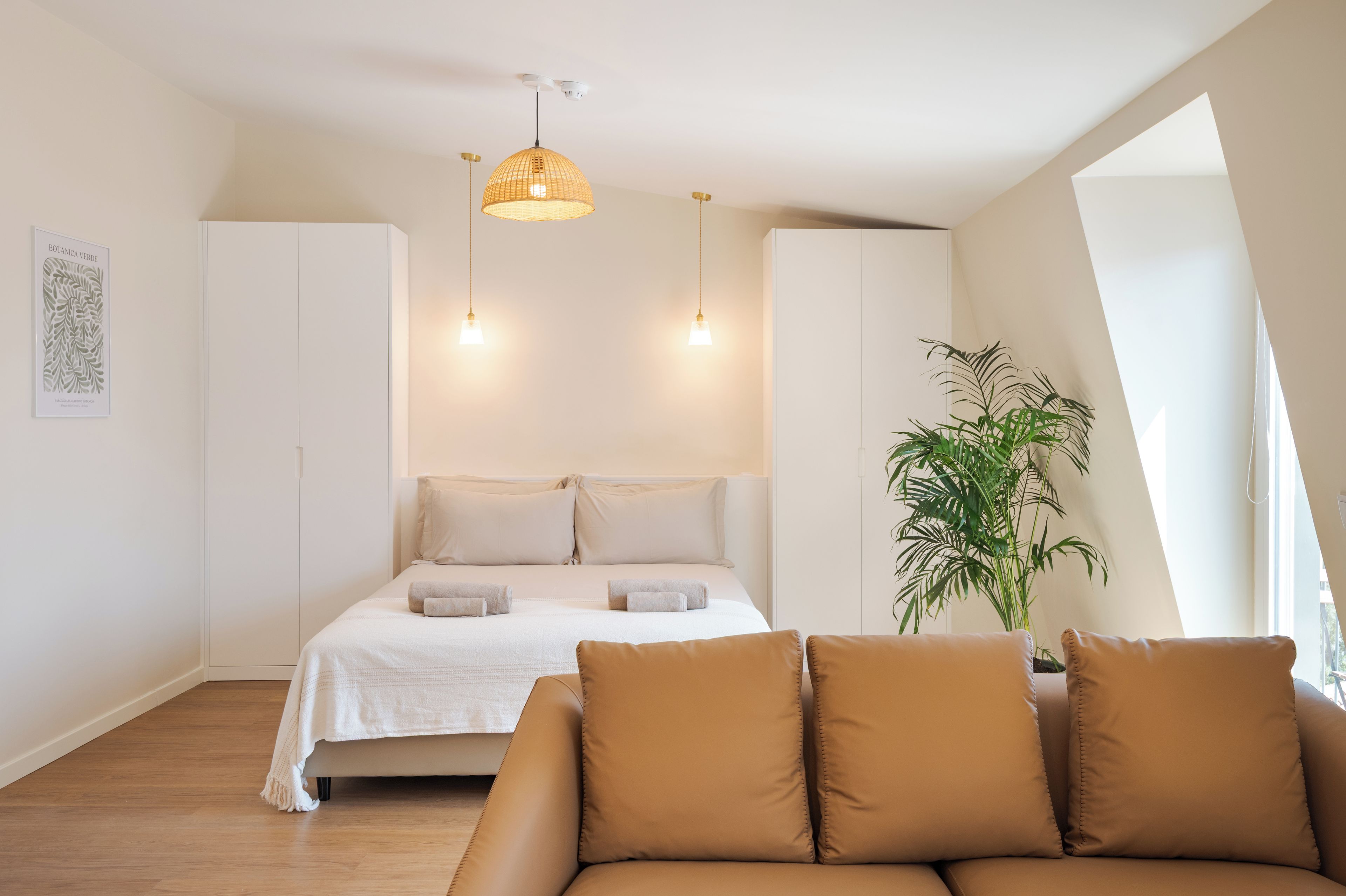 A modern bedroom with a bed, a sofa, a hanging light fixture, and a potted plant.