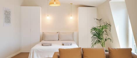 A modern bedroom with a bed, a sofa, a hanging light fixture, and a potted plant.