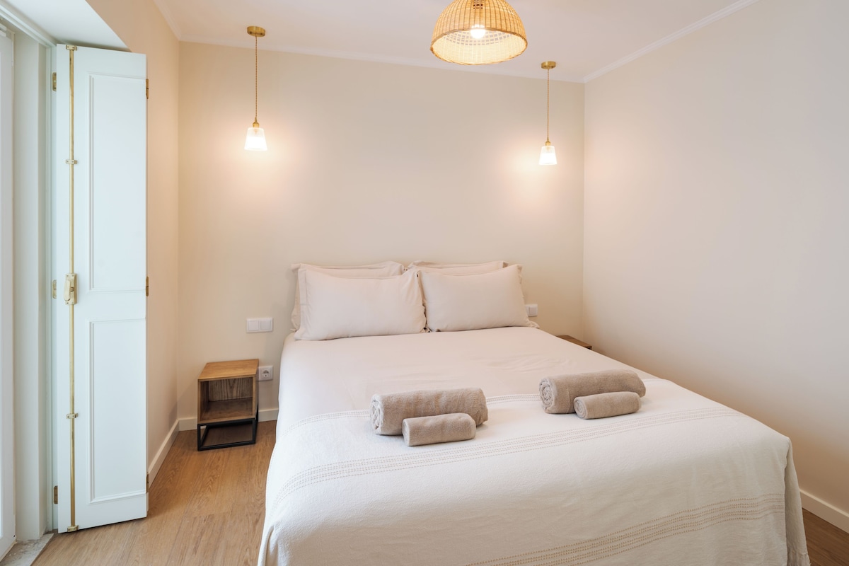 A bedroom with a bed, two bedside lamps, a nightstand, and a door.