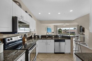 A modern kitchen with a central island, white cabinetry, and a view to the outside. - 3 Story Destin Villa | Private Beach | Shared Pool (Destin)