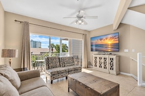 A living room with a sofa, coffee table, and a TV on a cabinet. There is a balcony with a view of the city. - 3 Story Destin Villa | Private Beach | Shared Pool (Destin)
