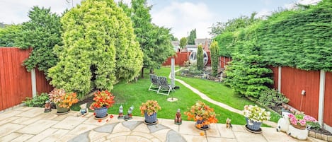 A garden patio with a stone floor, surrounded by a red fence, and various potted plants and garden statues.