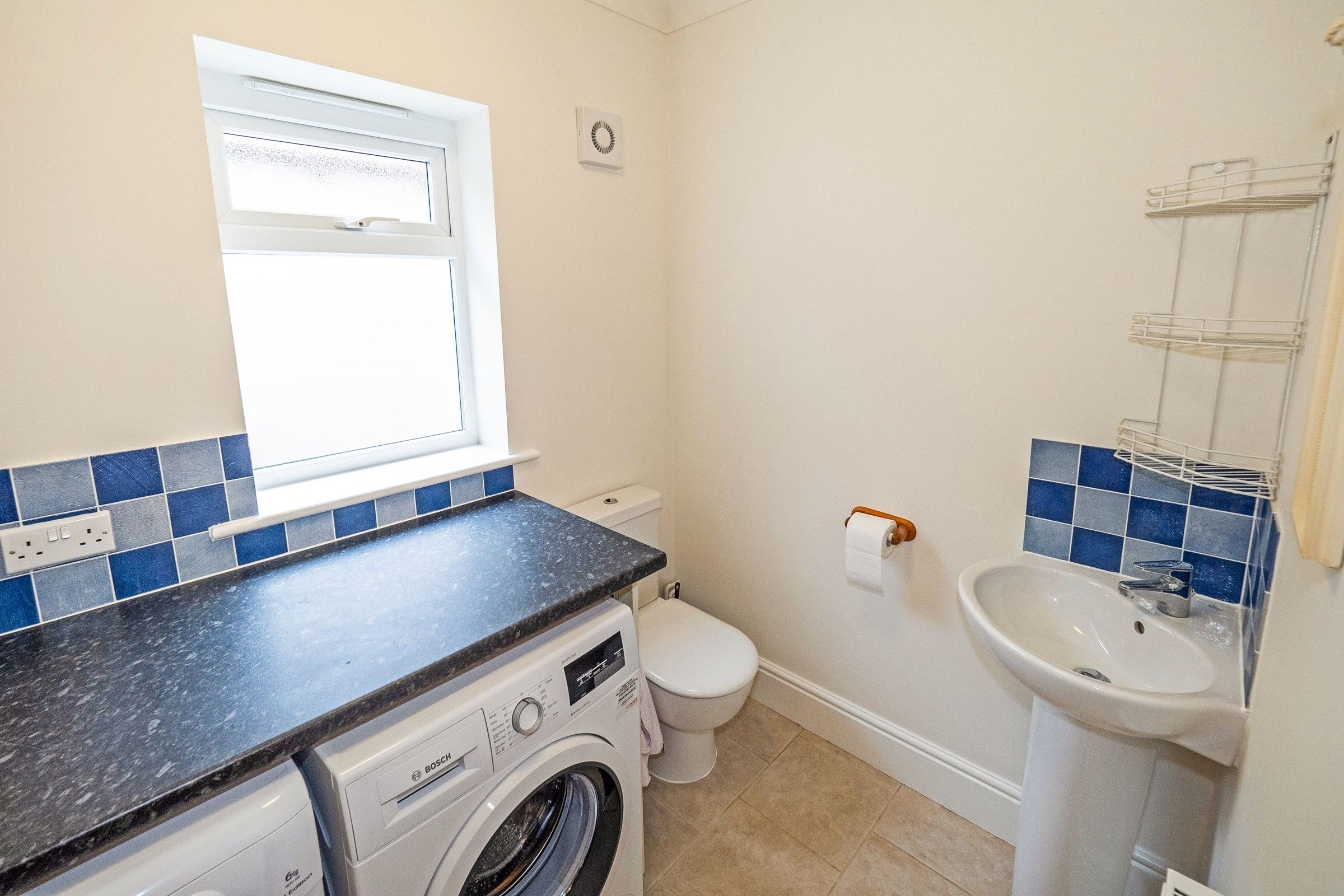 A compact bathroom with a washing machine, toilet, sink, and a window.