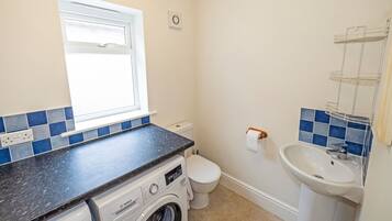 A compact bathroom with a washing machine, toilet, sink, and a window.